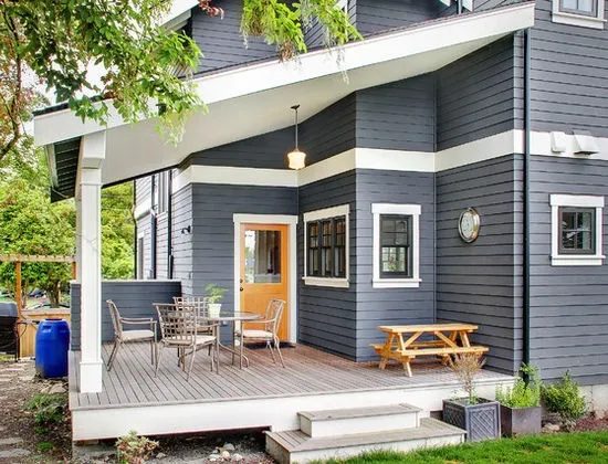 Home painted dark blue gray with white trim, beside a wood deck set with a table and chairs