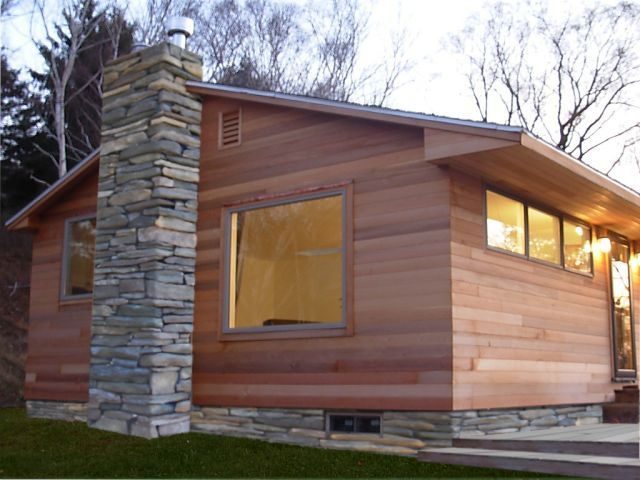 Cedar sided home with a stacked stone chimney and lit windows