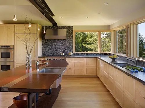 Kitchen with light wood cabinets, dark stone counters, and wide windows looking out to trees