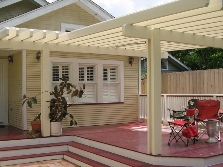 White pergola attached to a yellow house over a red deck