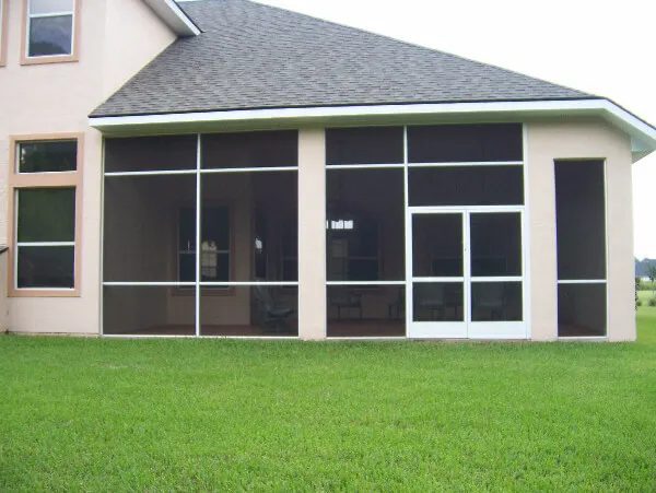 Screened porch enclosure across the back of a tan stucco home with patio furniture inside
