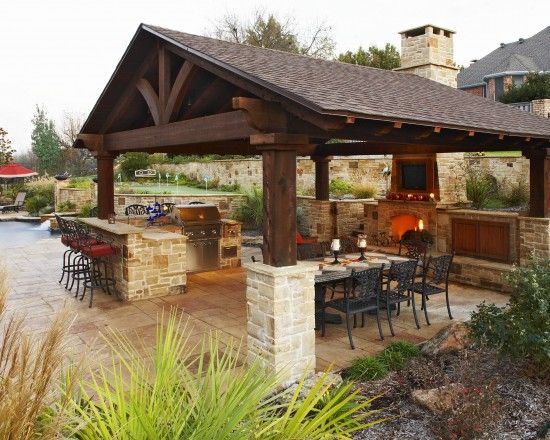 Freestanding timber pavilion with bar seating and a stone fireplace in a back yard