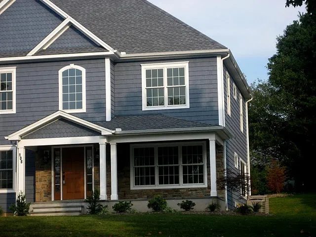Two story home with blue gray siding, white trim, stone accents and a covered entry with a wood front door