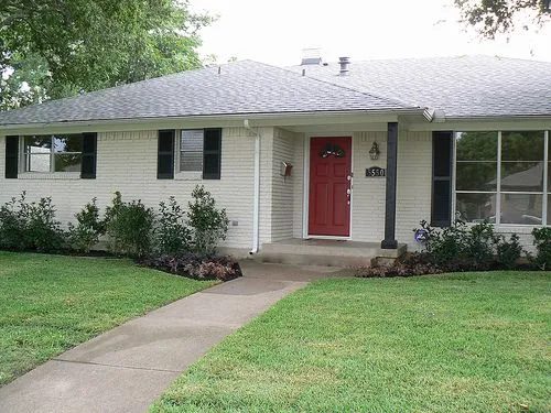 Single story white painted brick ranch home with a bright red front door and black shutters