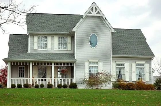 Two story white clapboard farmhouse with a covered front porch, shutters and an oval gable window