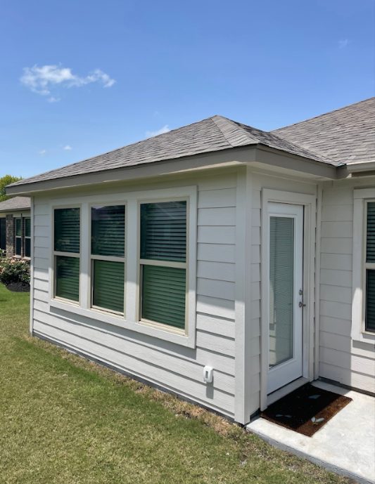 Finished room addition in white siding with a door and three windows