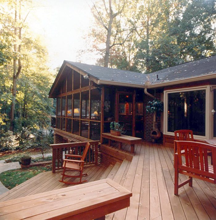 House with a wide wooden deck and red chairs under the eaves